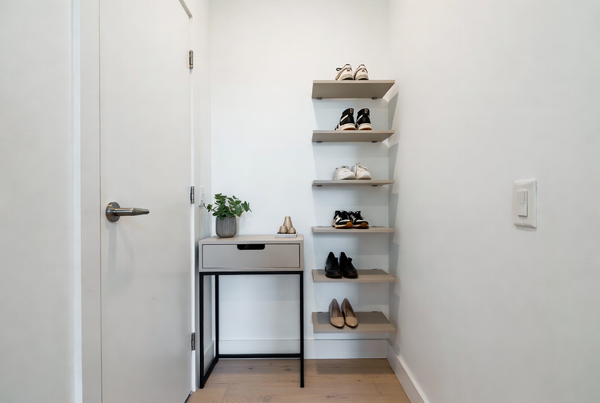 A bright modern entryway of a small apartment featuring a slim console table and wall-mounted floating ledges displaying neatly organized shoes, demonstrating creative shoe storage ideas for small spaces.